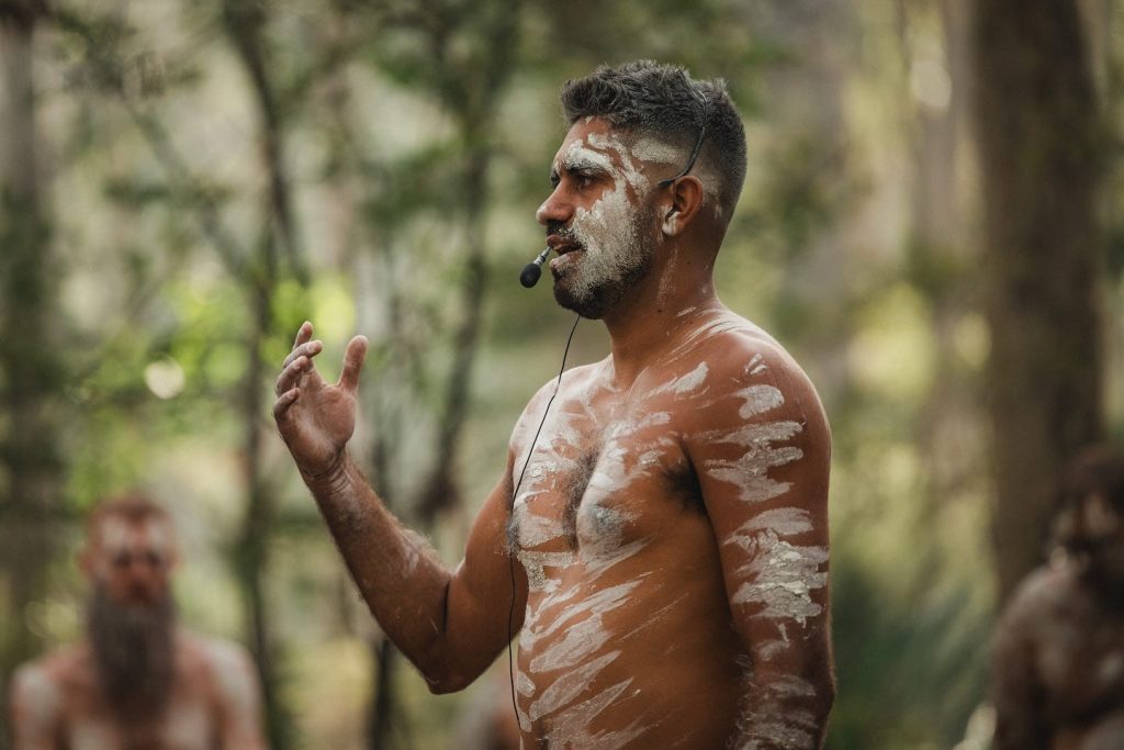 Aboriginal cultural presenter with traditional ochre body paint sharing stories at a cultural organization event